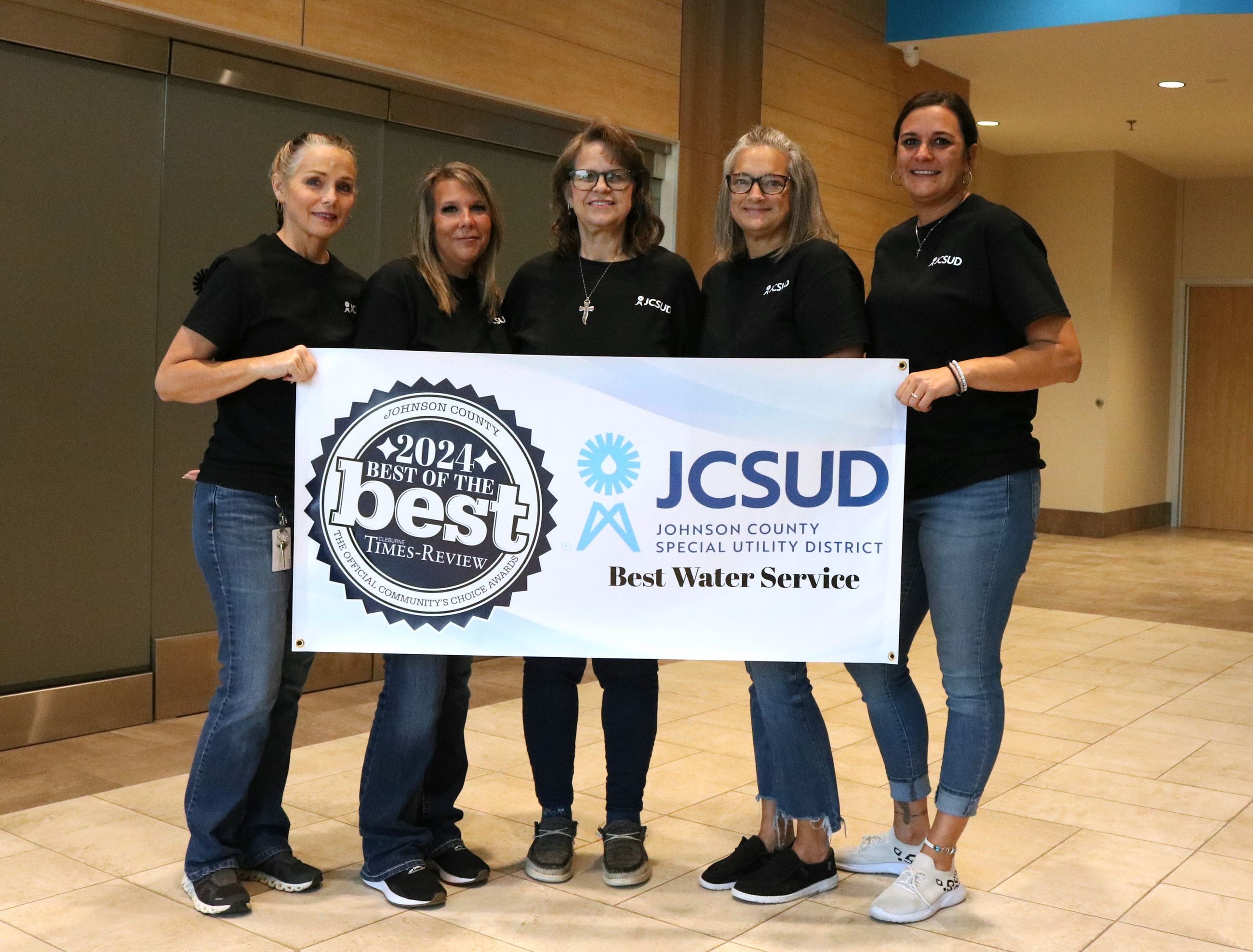 Group of JCSUD customer service staff standing together holding a banner